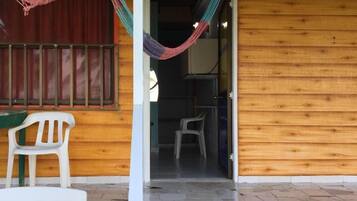 Un edificio de madera con un patio de baldosas, una silla de plástico blanca y una hamaca.