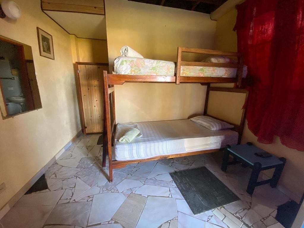 A small, compact room with a bunk bed, a single bed, a small table, and a shower area.