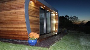 A modern wooden cabin with a glass door entrance, a blue flower pot, and a well-lit exterior. - The Pod Luxury Accommodation (Aberaeron)