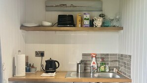 A kitchen with wooden shelves, a kettle, a sink, and various kitchen items. - The Pod Luxury Accommodation (Aberaeron)