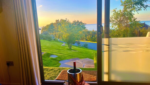 A room with a large window offering a view of a grassy area and a body of water. - The Pod Luxury Accommodation (Aberaeron)