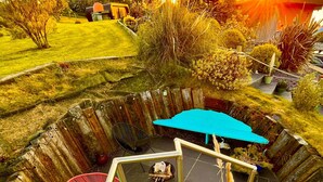 A spiral staircase with a blue umbrella and a red chair, surrounded by a garden with various plants and a wooden fence. - Luxury Pods - Sleeps 2 & Free Parking (Aberaeron)