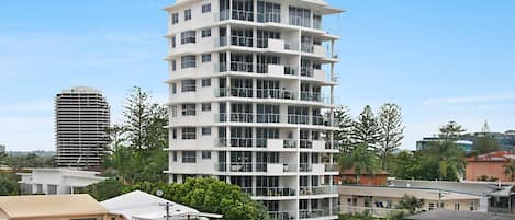 A multi-story building with balconies, surrounded by other buildings and greenery.
