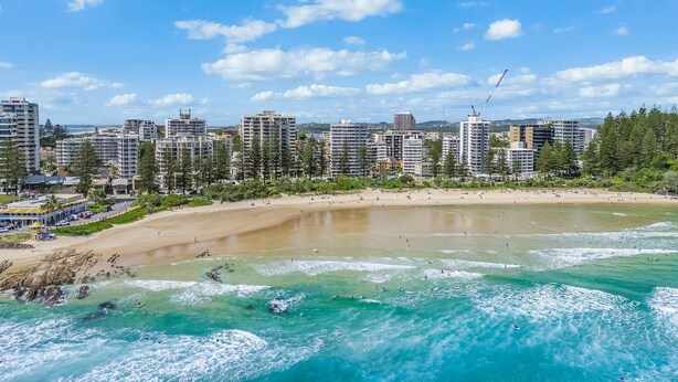 A coastal cityscape with a sandy beach, ocean waves, and high-rise buildings in the background.