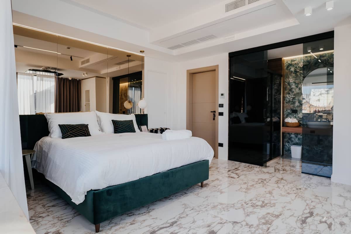 A modern bedroom with a large bed, a dark green upholstered headboard, and a marble floor.