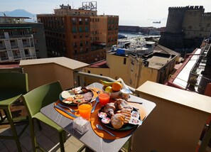 A balcony with a table set for breakfast, overlooking a cityscape with buildings and a castle. - POETICA BOUTIQUE SKY HOTEL (Naples)