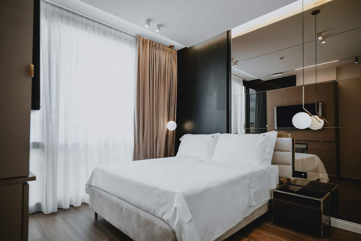 A modern hotel room with a large bed, a bedside table, a mirror, and a TV.