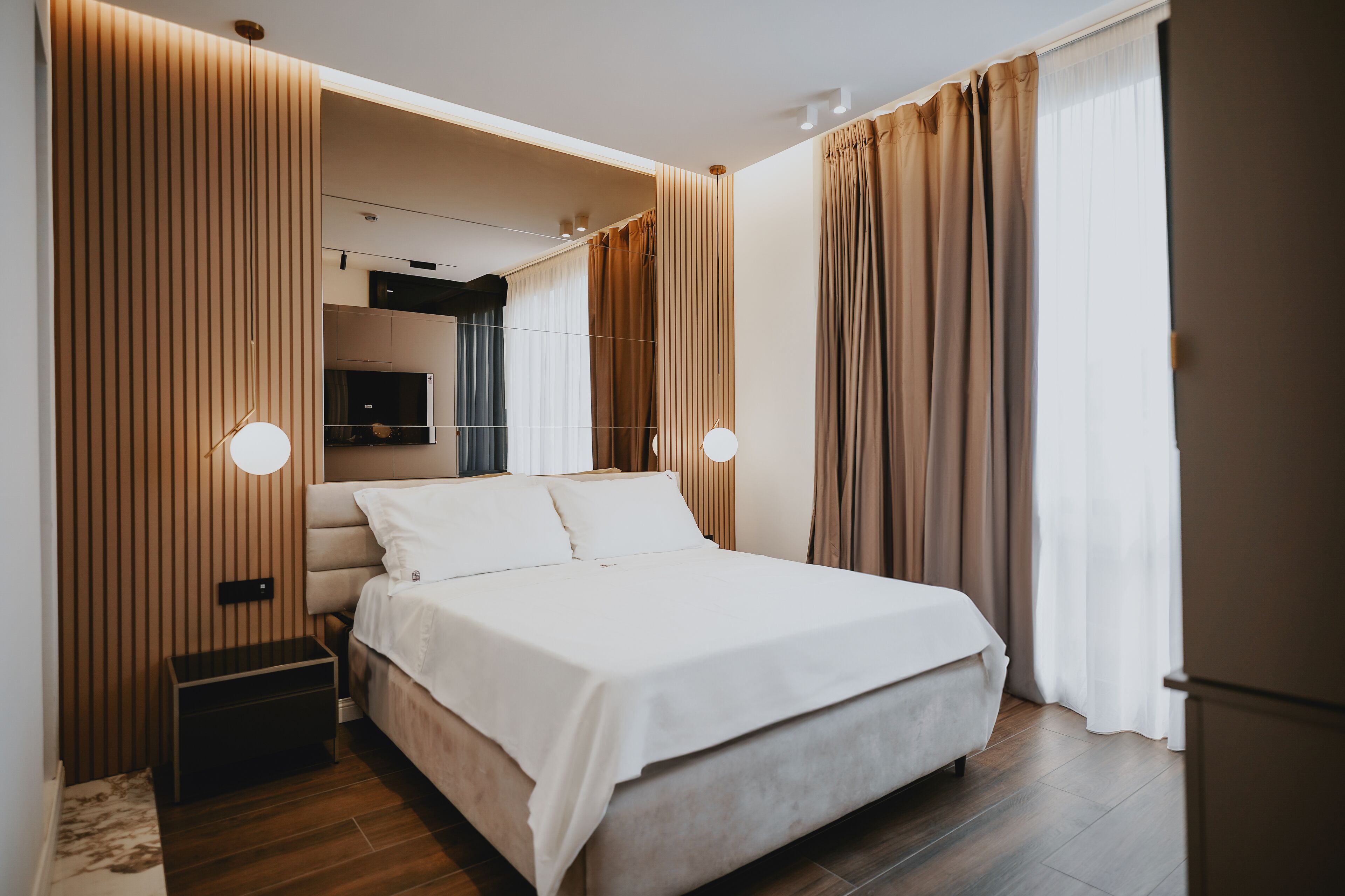 A modern bedroom with a large bed, wooden paneling, a TV, and a bedside table.