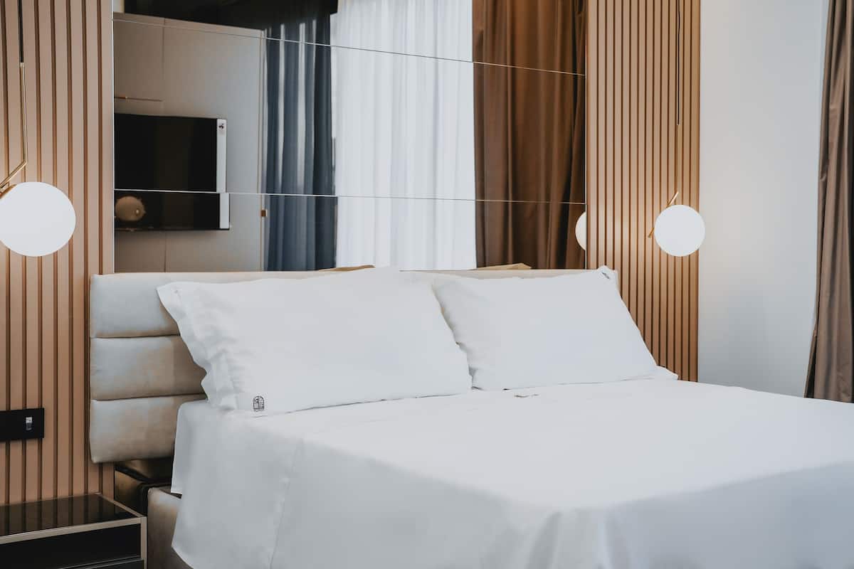 A neatly made bed with white linens in a modern room with wooden paneling and a built-in TV.