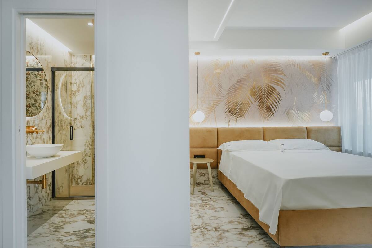 A modern bedroom with a large bed, a bedside table, a mirror, and a bathroom with a sink and shower.