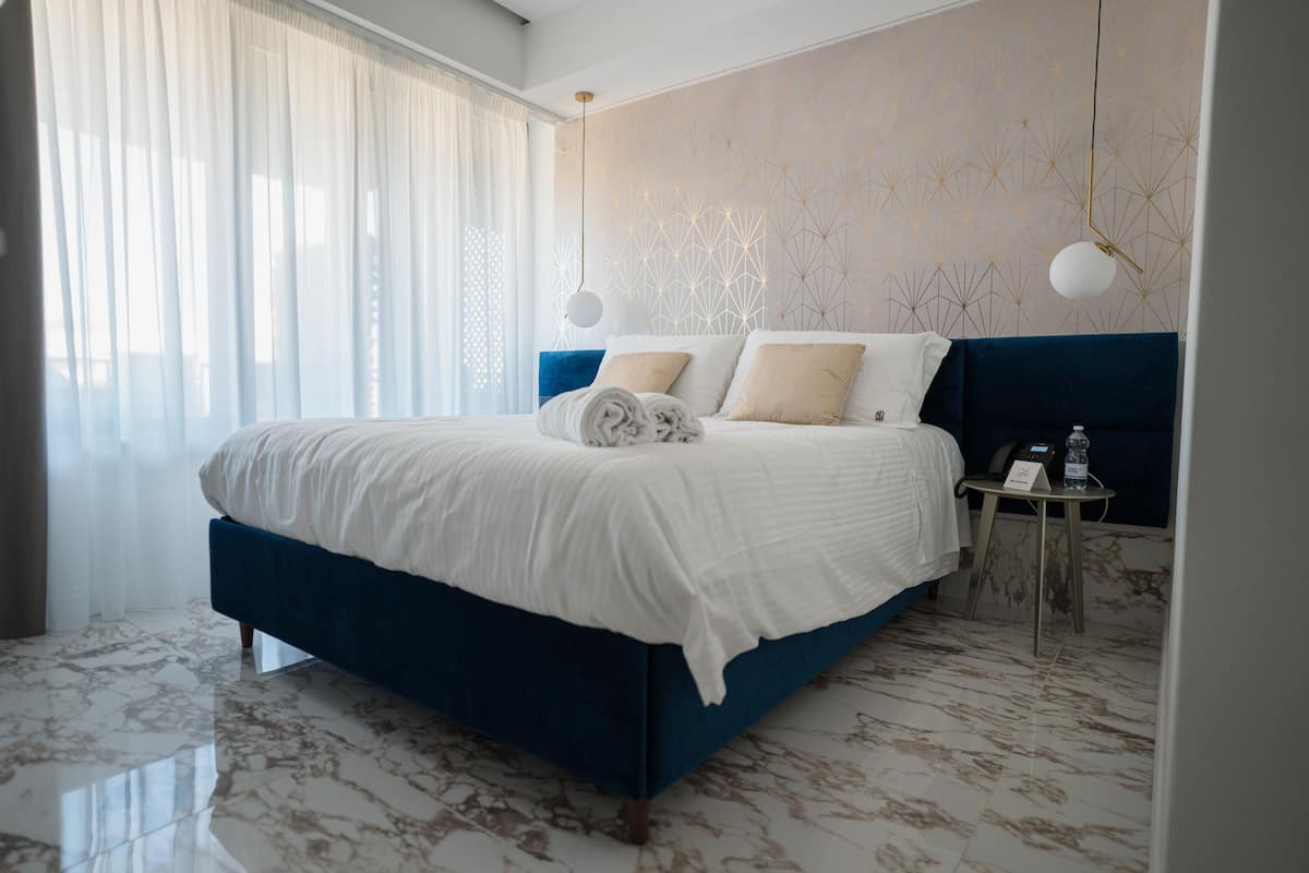 A modern hotel room with a large bed, marble flooring, and a decorative wall pattern.