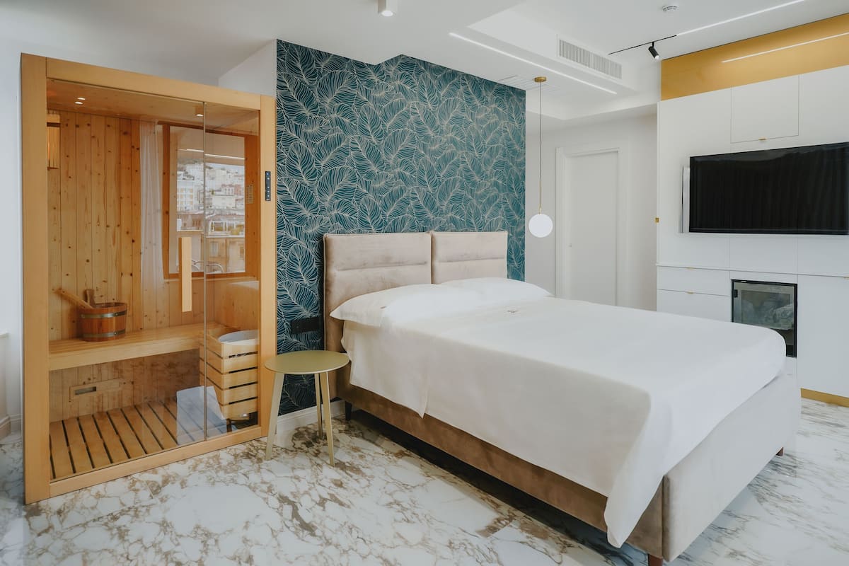 A modern bedroom with a large bed, a wooden wardrobe, a small table, a TV, and a wall with a leaf pattern.