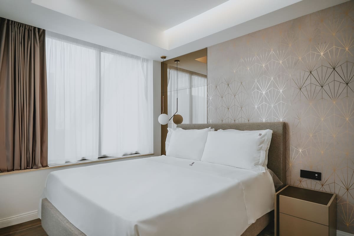 A modern hotel room with a large bed, a bedside table, and a wall with geometric patterns.