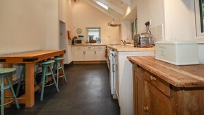 Uma cozinha com mesa de madeira, banquetas, micro-ondas, torradeira e uma janela.