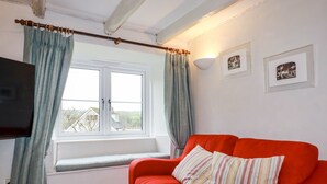 Quarto com sofá vermelho, janela com cortinas, televisão fixada na parede e duas imagens emolduradas.