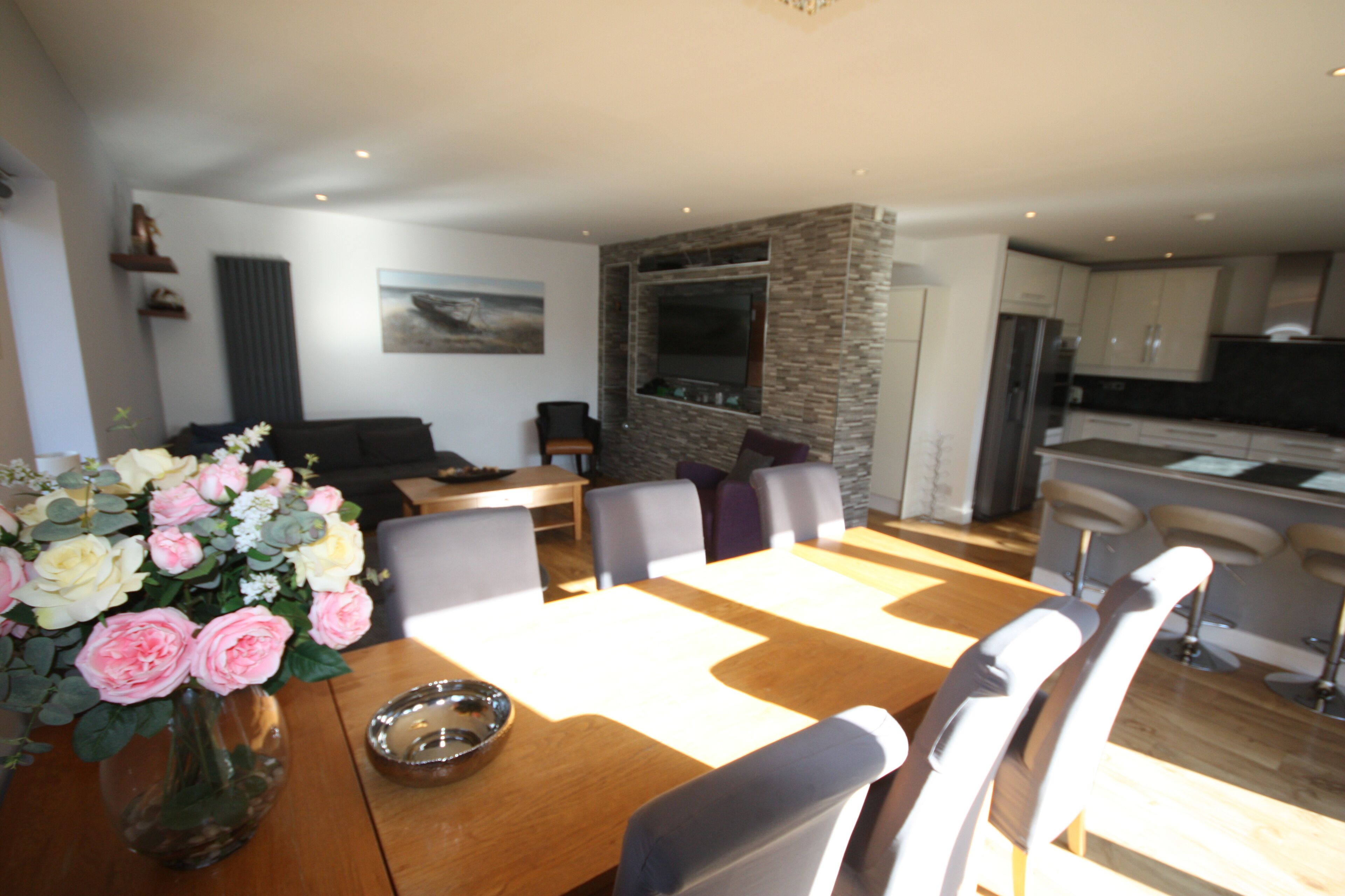 A dining area with a wooden table, chairs, a vase of flowers, and a stone accent wall.