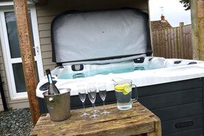 A hot tub with a wooden table in front, a bucket with a bottle, and four glasses.