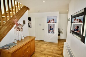 A hallway with a wooden staircase, a white door, and a wall with framed photos.