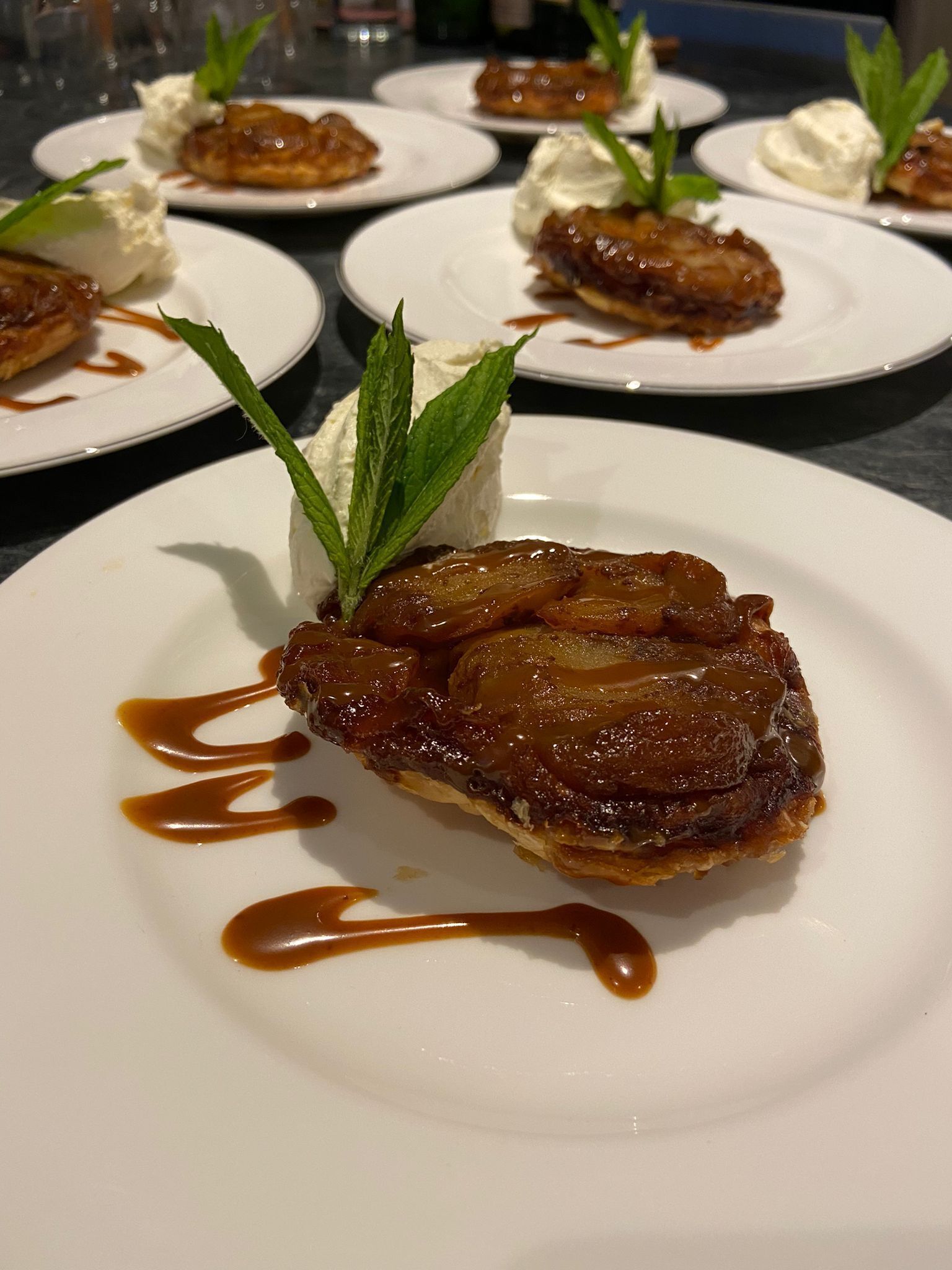 A dessert plate with caramelized fruit on top, garnished with mint leaves and drizzled with caramel sauce.