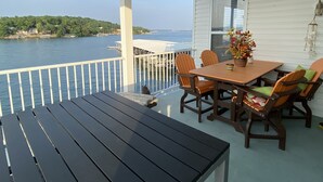 A covered outdoor area with a table and chairs, a view of the water, and a white building with a window.