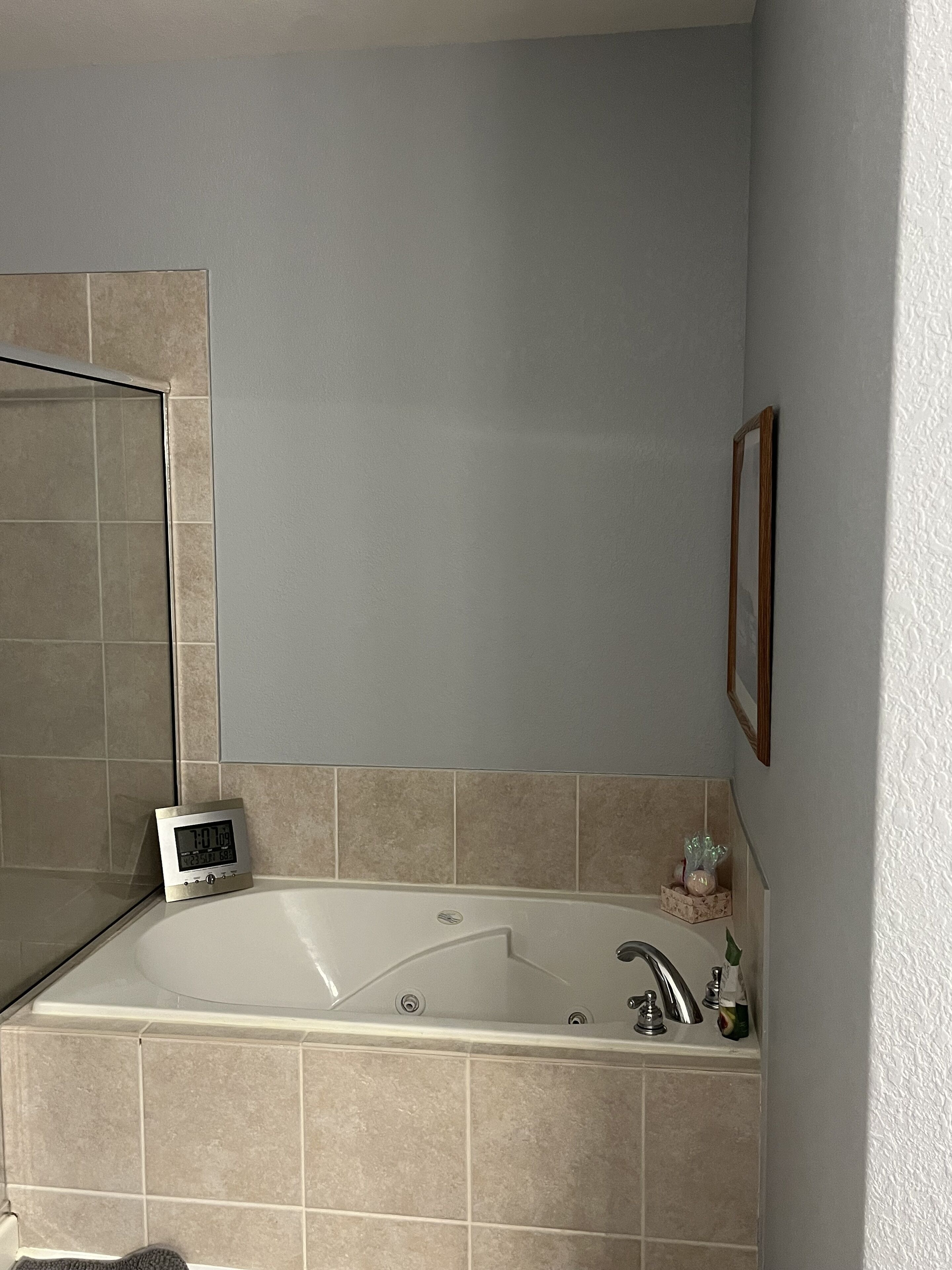 Un baño con bañera, un reloj digital y un cuadro en la pared.