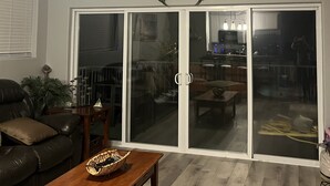 A living room with a ceiling fan, a decorative crab wall art, a sliding glass door leading to a dining area, and a leather sofa.