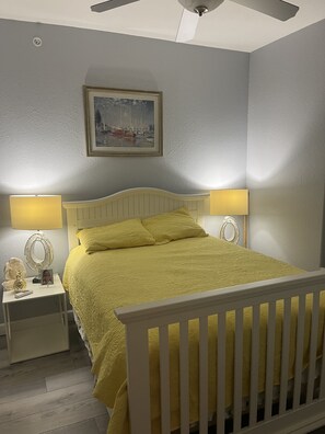 Quarto com cama, duas luminárias de cabeceira, ventoinha no teto e um quadro na parede.