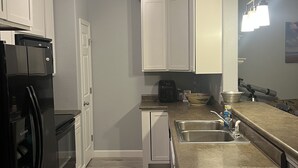 A compact kitchen with white cabinets, a black refrigerator, a coffee maker, and a sink.