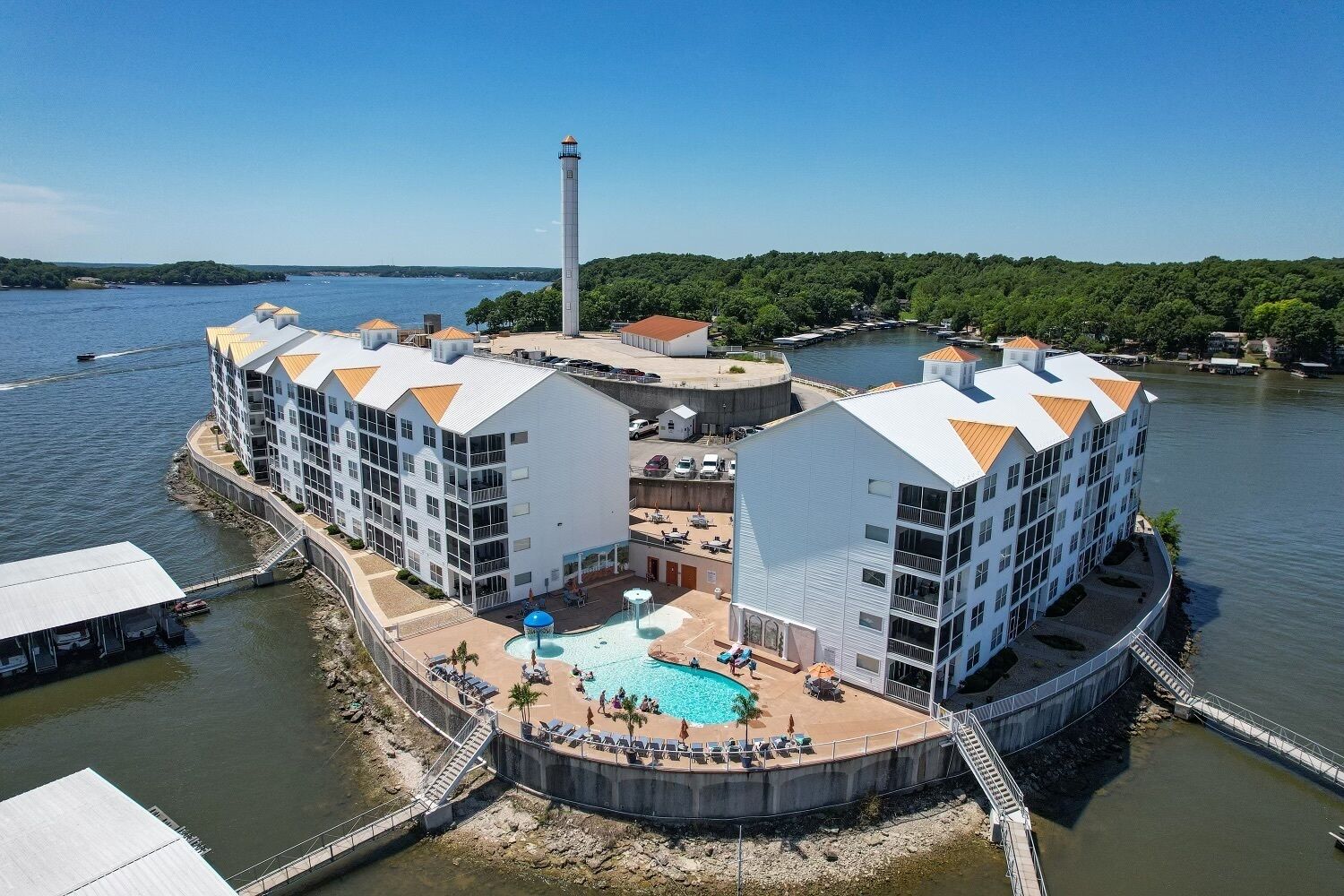 A waterfront hotel with multiple buildings, a swimming pool, and a lighthouse in the background.