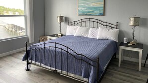 A bedroom with a bed, two bedside tables, a window with a view of a dock, and a painting on the wall.