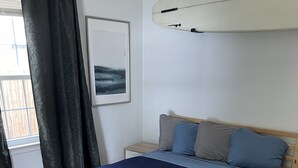 A bedroom with a wooden bed frame, a blue bedspread, and a nightstand with a drawer. - The Modern beach bungalow. 7 minutes to ocean front, full private home!  (Virginia Beach)