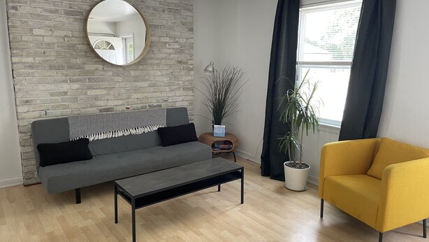 A modern living room with a grey sofa, a yellow armchair, a coffee table, a round mirror, and a potted plant. - The Modern beach bungalow. 7 minutes to ocean front, full private home!  (Virginia Beach)