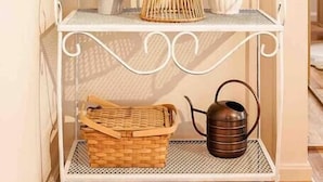 A white metal shelf with various items including plants, a wicker basket, a vase, and a teapot. - The Golden Suite: themed getaway! (Cincinnati)