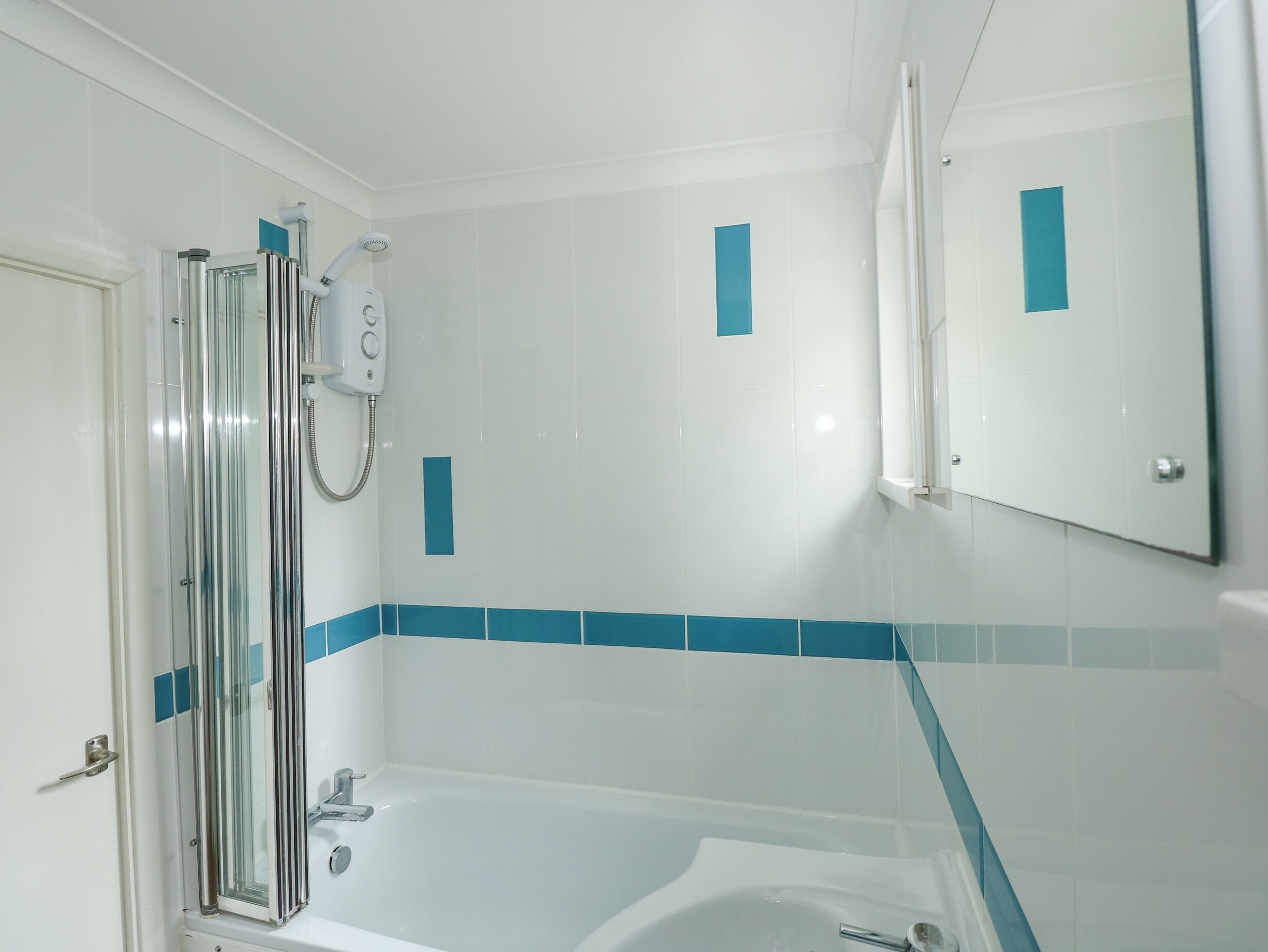 Een badkamer met een douche met glazen wand, een wit ligbad en blauwe betegelde wanden.