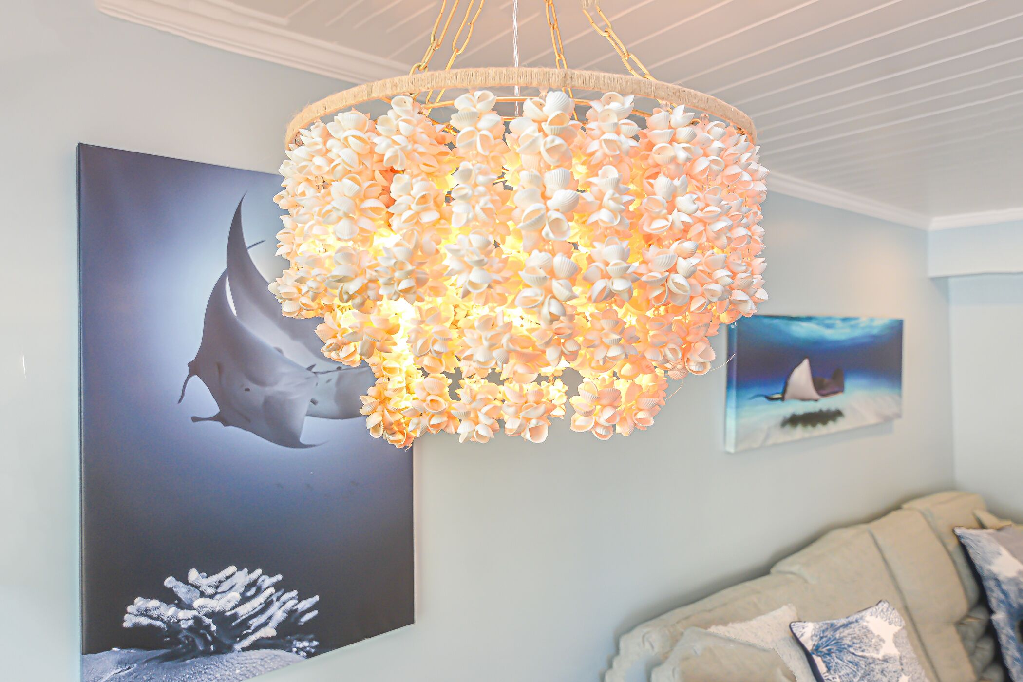 A chandelier with a floral design, a large framed picture of a shark, and a couch with pillows.