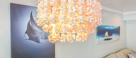 Um candelabro com detalhes florais, uma grande moldura com a imagem de um tubarão e um sofá com almofadas.