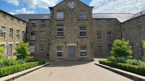 A historic stone building with a clock tower, large windows, and a central door. - Millnook (Harrogate)