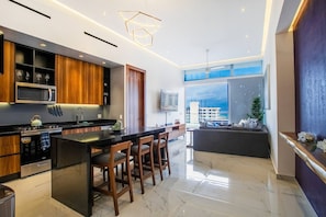 A modern kitchen with a central island, wooden cabinets, and a large window offering a city view.