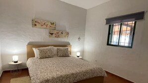 A bedroom with a bed, two bedside lamps, a window with bars, and a wall with a floral artwork. - Bed&ride, Modern Country Apartment Telde (Ojos de Garza)