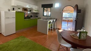 A compact kitchen with a green accent wall, a dining area with a wooden table, and a view through an open door. - Bed&ride, Modern Country Apartment Telde (Ojos de Garza)