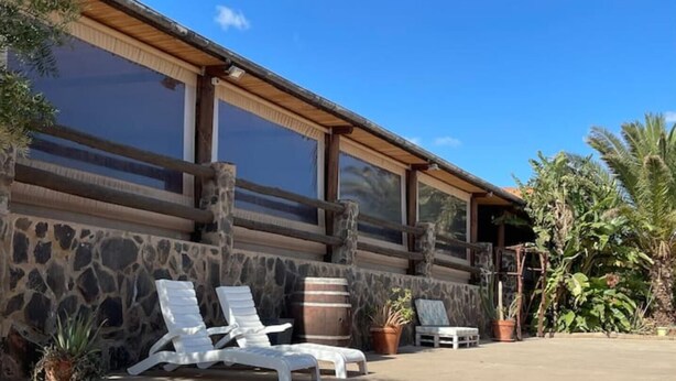 A building with a stone facade, large windows, and a patio area with lounge chairs and potted plants. - Bed&ride, Modern Country Apartment Telde (Ojos de Garza)