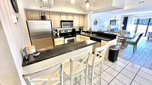 A modern kitchen with a central island, stainless steel appliances, pendant lighting, and a dining area with a view. - New Rental, Beautiful villa with relaxing views! 912HP (Miramar Beach)