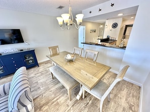 A dining area with a wooden table, cushioned chairs, a blue cabinet, and a TV on the wall.