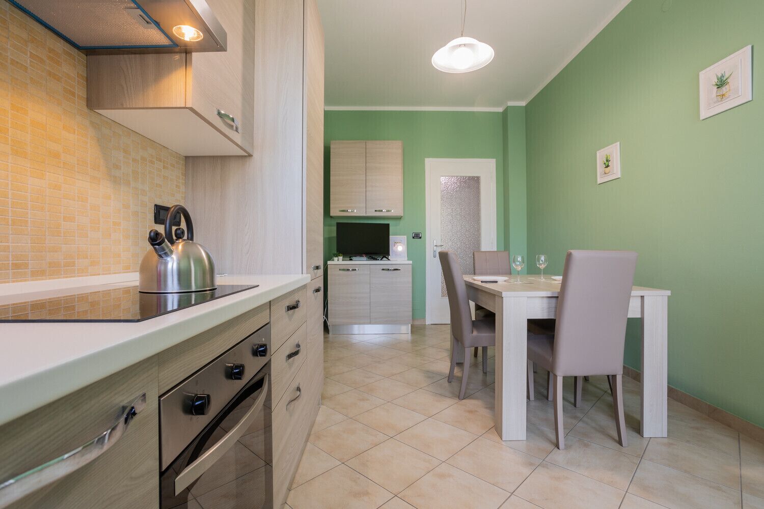 A modern kitchen with a dining area, featuring a kettle, cabinets, and a table with chairs.