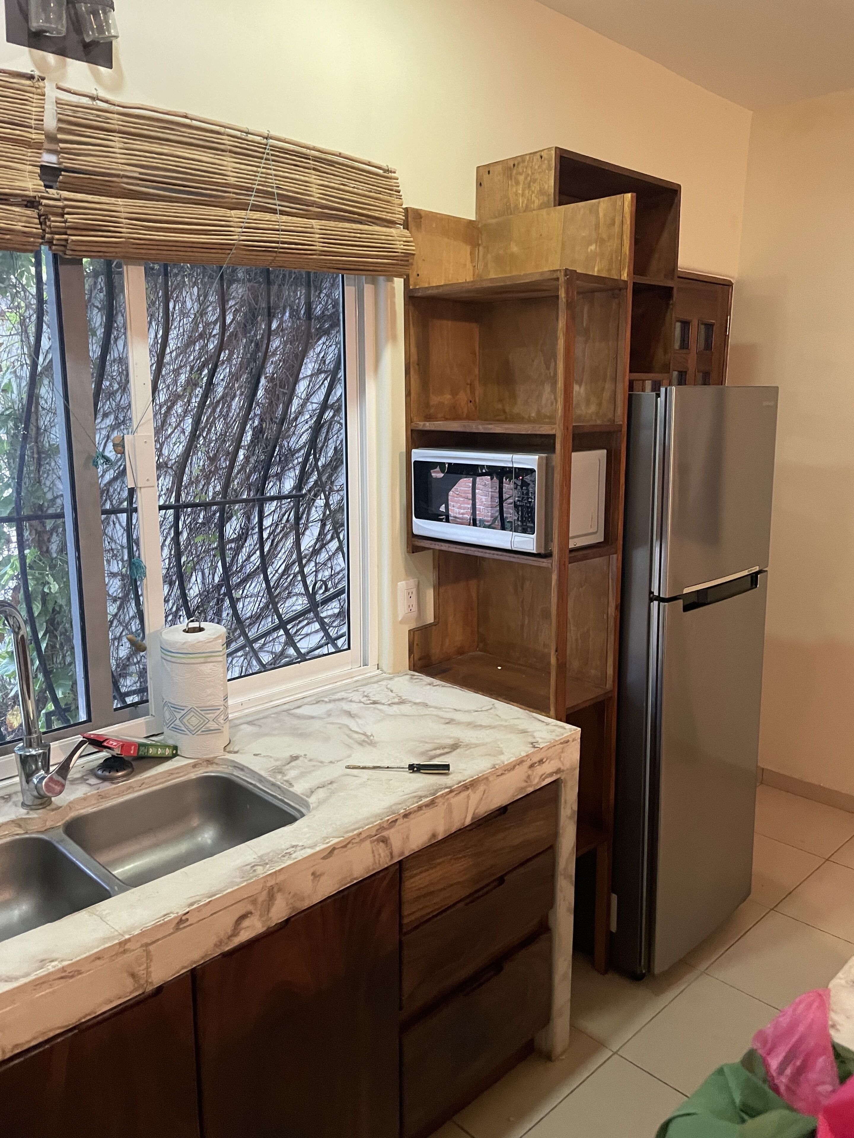 A kitchen with a marble countertop, wooden cabinets, a stainless steel refrigerator, and a microwave on a wooden shelf.