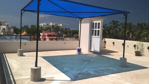 Una terraza en la azotea con toldo azul, una puerta y vistas a edificios y palmeras.
