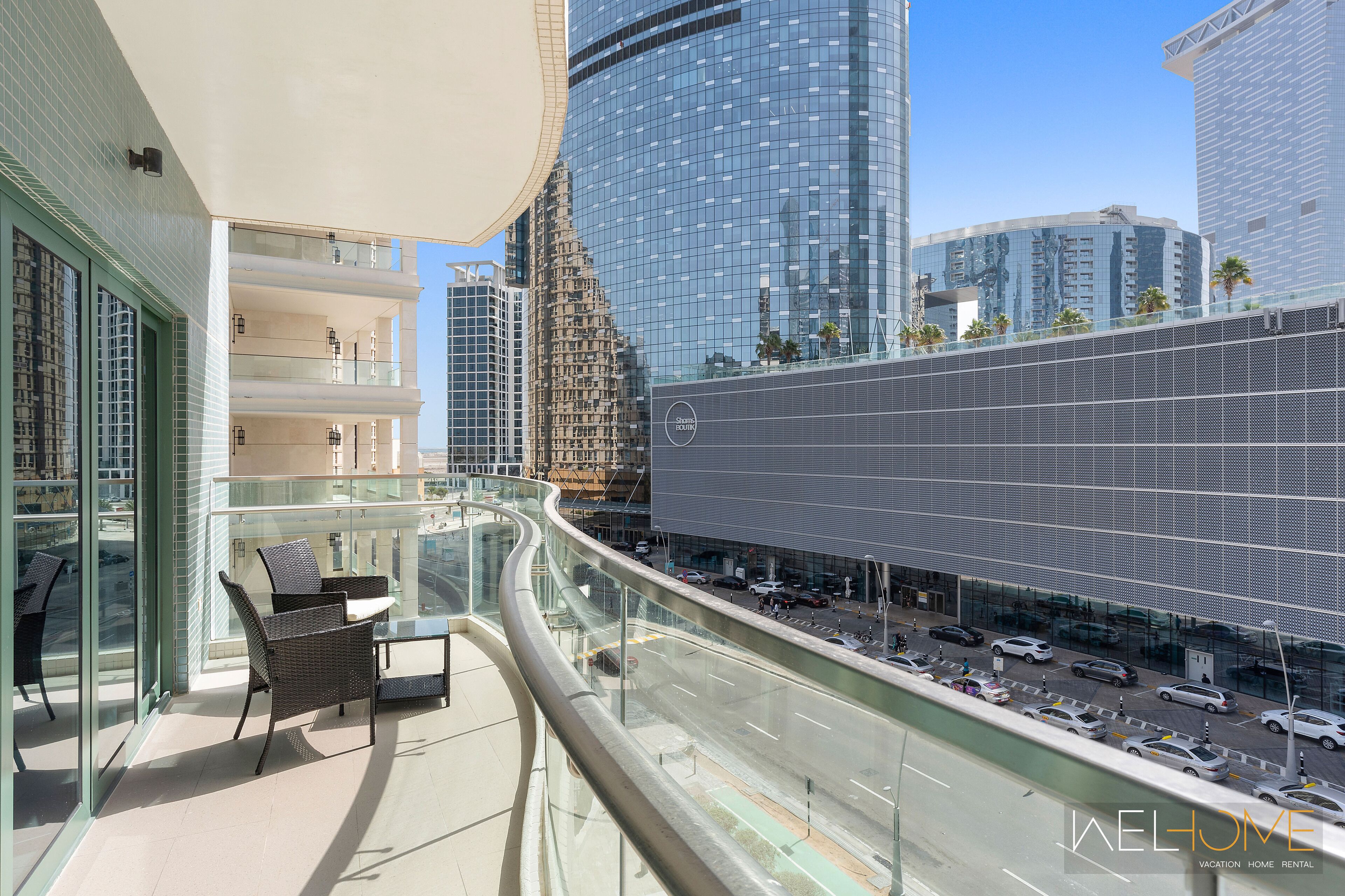 A modern hotel with a glass balcony overlooking a busy street and tall buildings.