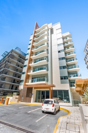 A modern multi-story hotel with a curved entrance and a white car parked in front. - WelHome - Reem Diamond Residence (Abu Dhabi)