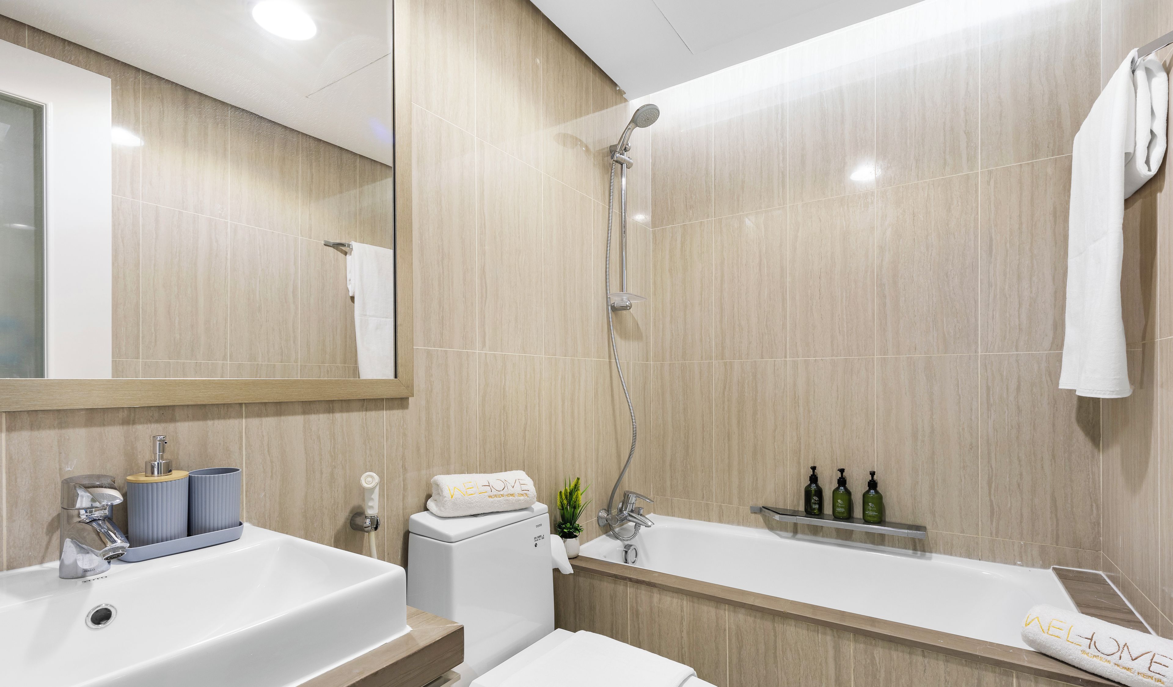 Ein modernes Badezimmer mit einem großen Waschbecken, Toilette und Badewanne. Auf dem Waschbecken liegen Toilettenartikel und der Handtuchhalter ist mit einem Handtuch versehen.