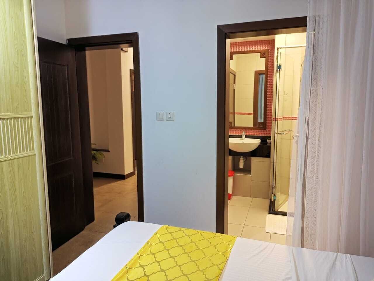 A hotel room with a bed, a bathroom visible through an open door, and a small plant in the corner.